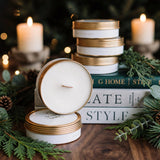 Stacked Gilded Rose and Spruce travel tin candles in a cozy holiday scene