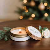 Lit Gilded Rose and Spruce travel tin candle with lid on dark walnut