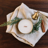 Gilded Rose and Spruce travel tin candle on natural linen with brass snuffer