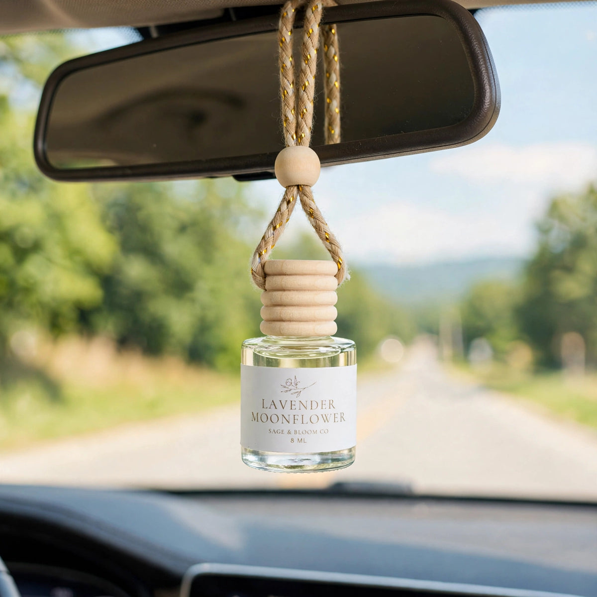 Lavender Moonflower car diffuser hanging from a rearview mirror on a summer drive