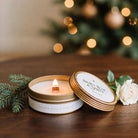 Lit Gilded Rose and Spruce travel tin candle with lid on dark walnut