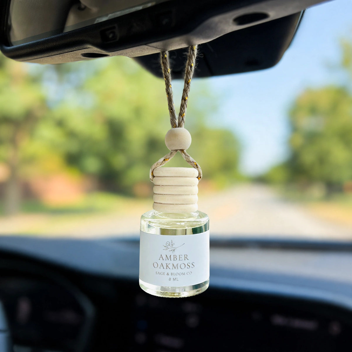 Amber Oakmoss car diffuser hanging from a rearview mirror on a summer drive