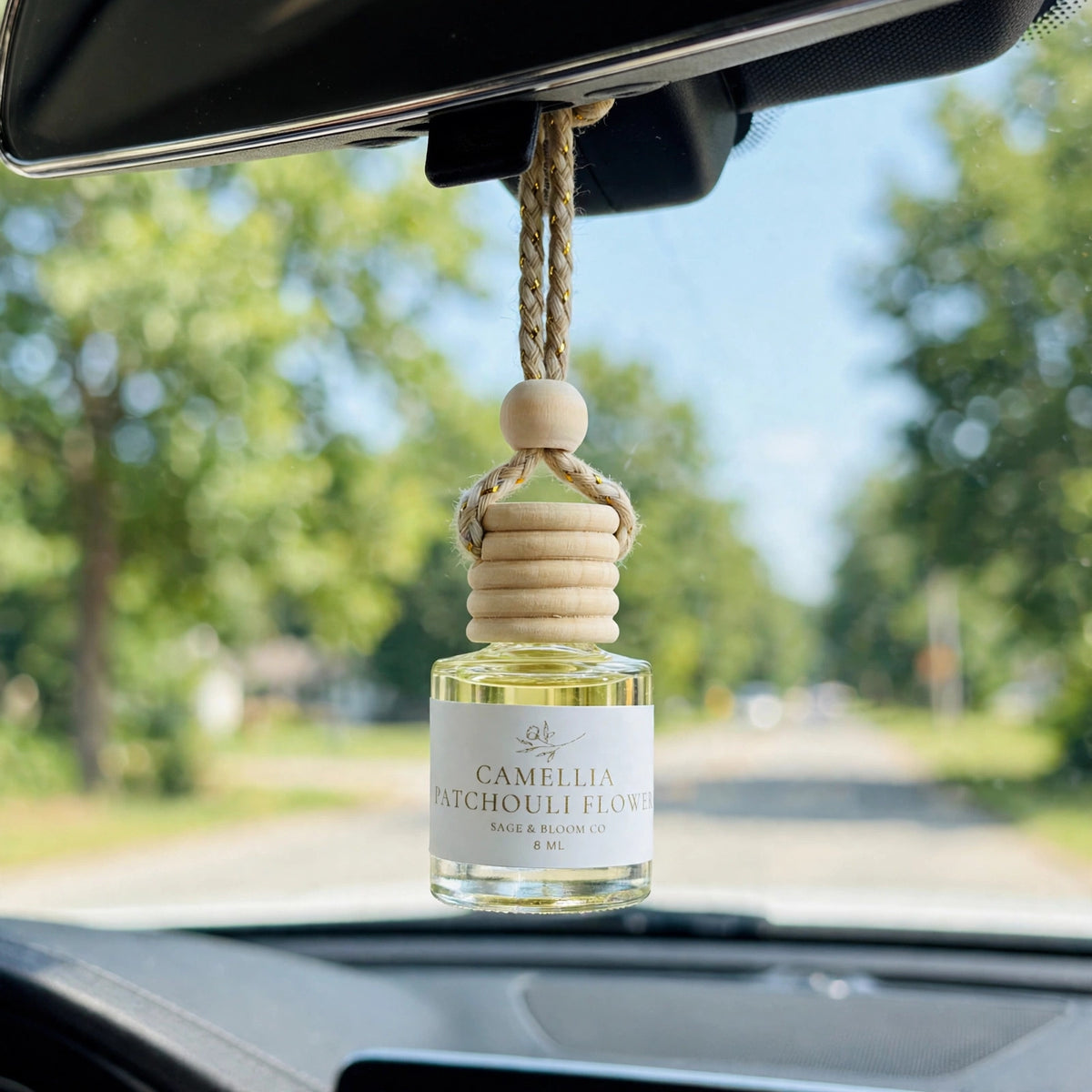 Camellia Patchouli Flower car diffuser hanging from a rearview mirror on a summer drive