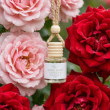 Dark Rose Vanilla car diffuser hanging among large close-up roses