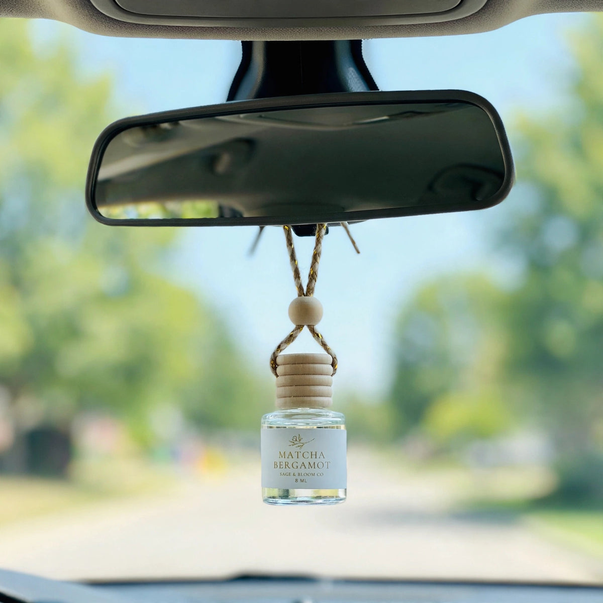 Matcha Bergamot car diffuser hanging behind the rearview mirror on a summer drive