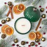 Top-down flatlay of Christmas ornament candle with dried oranges, cinnamon, and pine