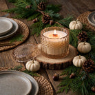 Vanilla Pumpkin Santal vintage glass candle lit on a woodsy dining table with white pumpkins and evergreen